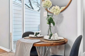 Un'area pranzo con un tavolo rotondo, due sedie, un vaso con fiori e uno specchio appeso al muro.