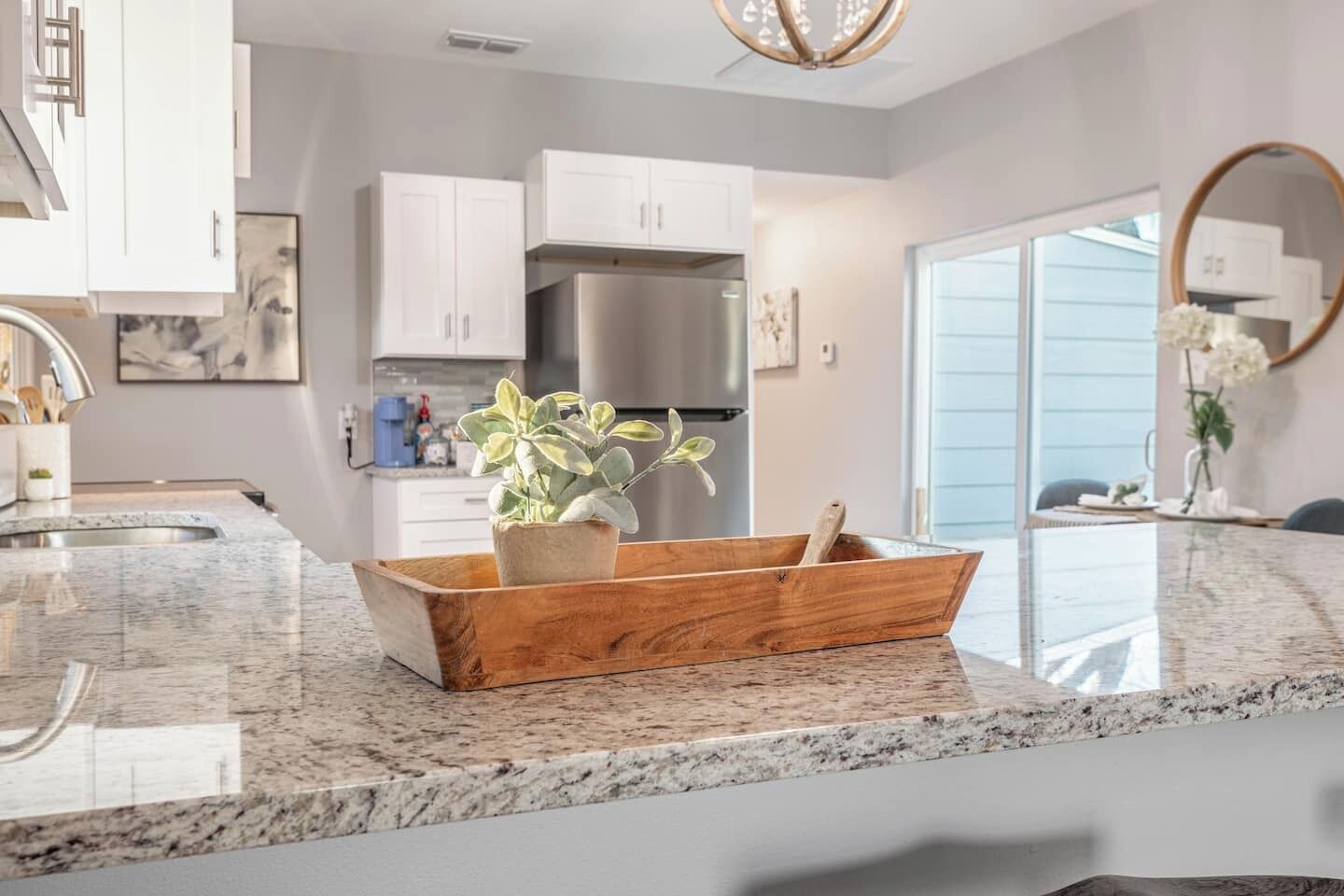 A modern kitchen with white cabinets, a stainless steel refrigerator, and a wooden plant stand on the granite countertop.