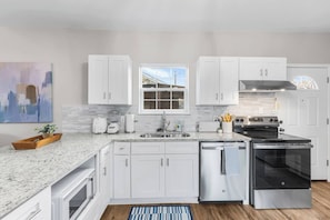 A modern kitchen with white cabinets, a built-in oven, a dishwasher, and a granite countertop. - NEW RENO! 4BR-2bath Modern Home | Central Location (Abilene)