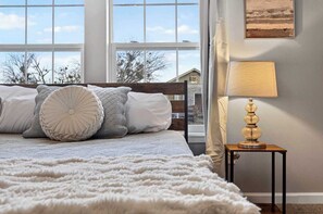 A bedroom with a large bed, a bedside lamp, and a view through the window.