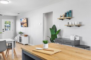 Une cuisine moderne avec un plan de travail en bois, un coin repas avec une table et des chaises blanches, et une grande plante verte.
