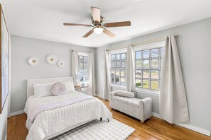 Une chambre à coucher avec un lit, une chaise, un ventilateur de plafond et de grandes fenêtres.