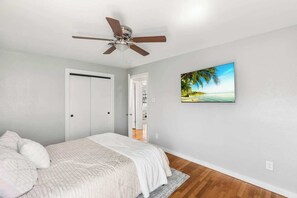 A bedroom with a bed, a ceiling fan, a white door, and a wall-mounted picture of a beach. - Bright & Stylish 3bed 2bath Abilene Home (Abilene)