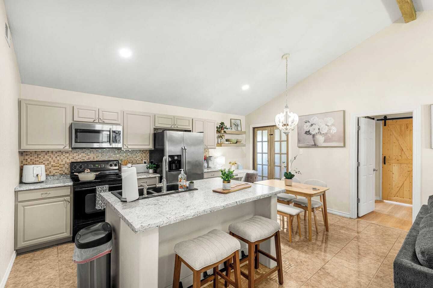 A modern kitchen with a central island, stainless steel appliances, and a dining area with wooden chairs.