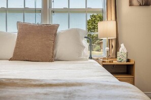 Ein ordentlich bezogenes Bett mit Kissen, einer Nachttischlampe und einer Taschentuchbox auf einem Holznachttisch.