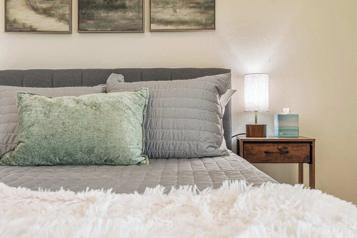 A bedroom with a bed, pillows, a nightstand, a lamp, and a wall-mounted picture.