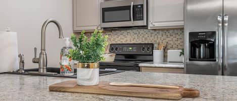 Una cocina con encimera de granito, electrodomésticos de acero inoxidable y tabla de cortar de madera.