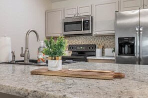 Eine Küche mit einer Granit Arbeitsplatte, Edelstahlgeräten und einem Holzb cutting board.