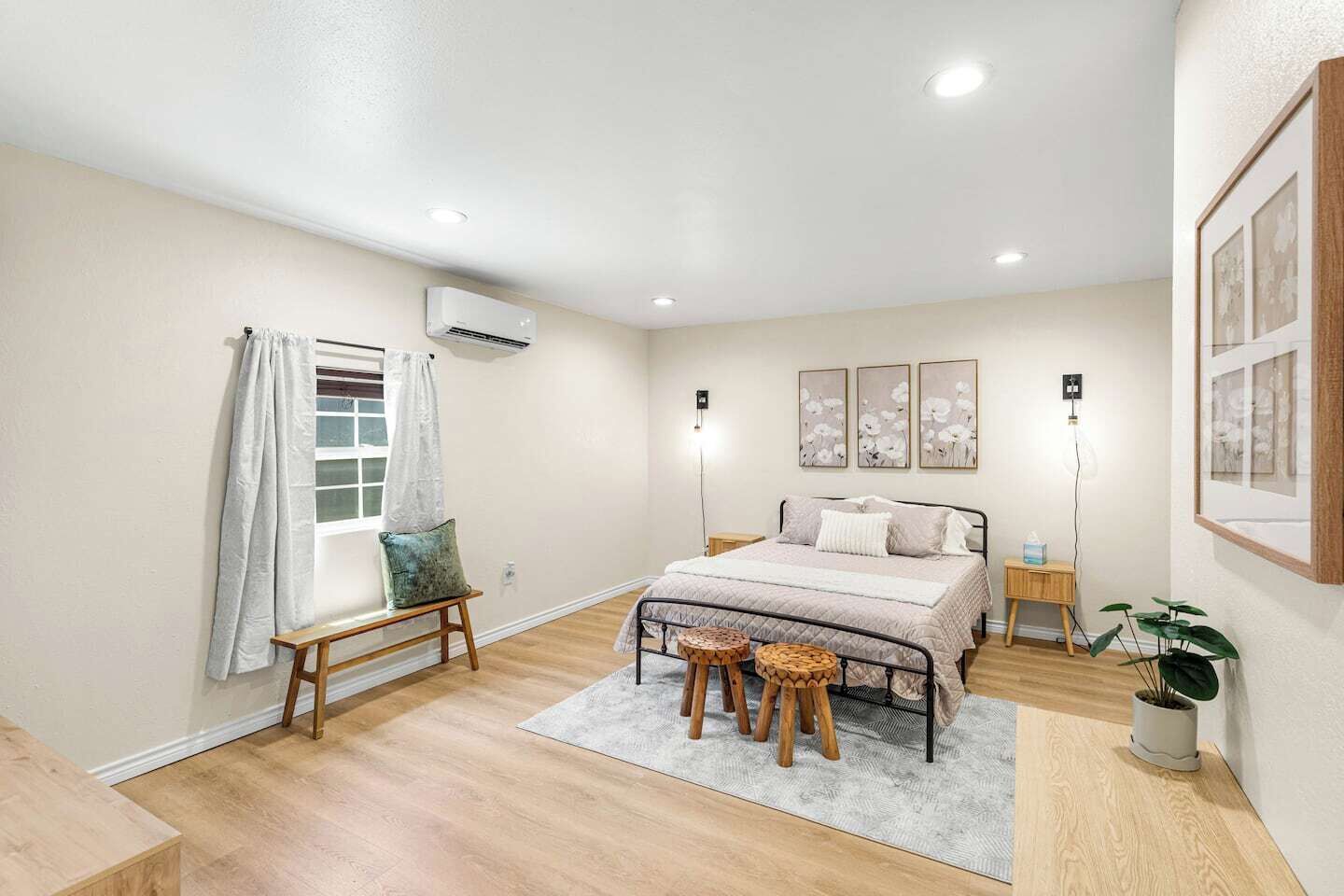 Een slaapkamer met een bed, nachtkastjes, een bankje, een potplant en kunst aan de muren.
