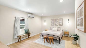 Een slaapkamer met een bed, nachtkastjes, een bankje, een potplant en kunst aan de muren.