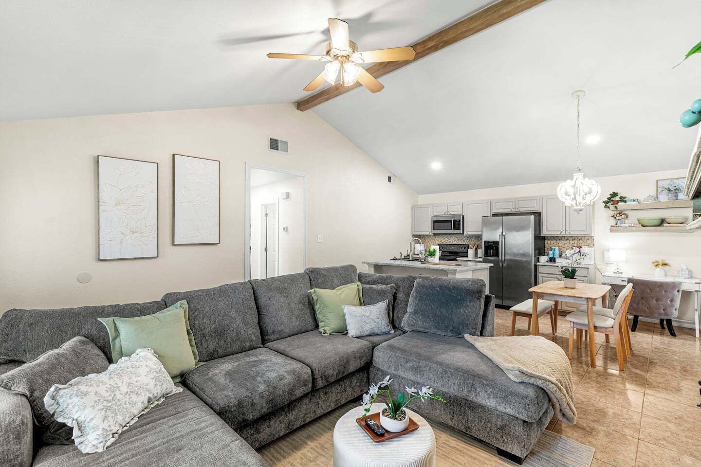 A modern living room with a grey sectional sofa, a small coffee table with a plant, and a dining area with a wooden table and chairs.