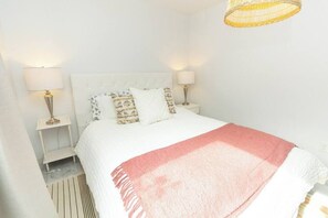 A bedroom with a white bed, two bedside tables with lamps, a patterned throw blanket, and a hanging light fixture.