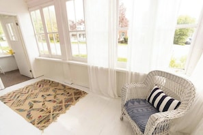 A room with a wicker chair, a patterned rug, and a view through large windows.