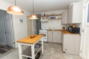 Cuina compacta amb taula de fusta, armaris blancs, fogó i microones.
