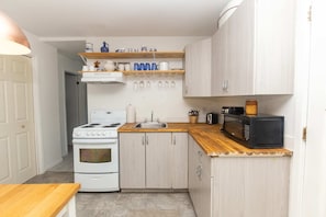 A compact kitchen with a white stove, a microwave, and a sink. There are wooden cabinets and a wooden countertop. - Best Location in Wellington, Prince Edward County (Prince Edward)