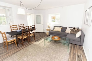 A modern living room with a dining table, chairs, a sofa, and a glass coffee table.