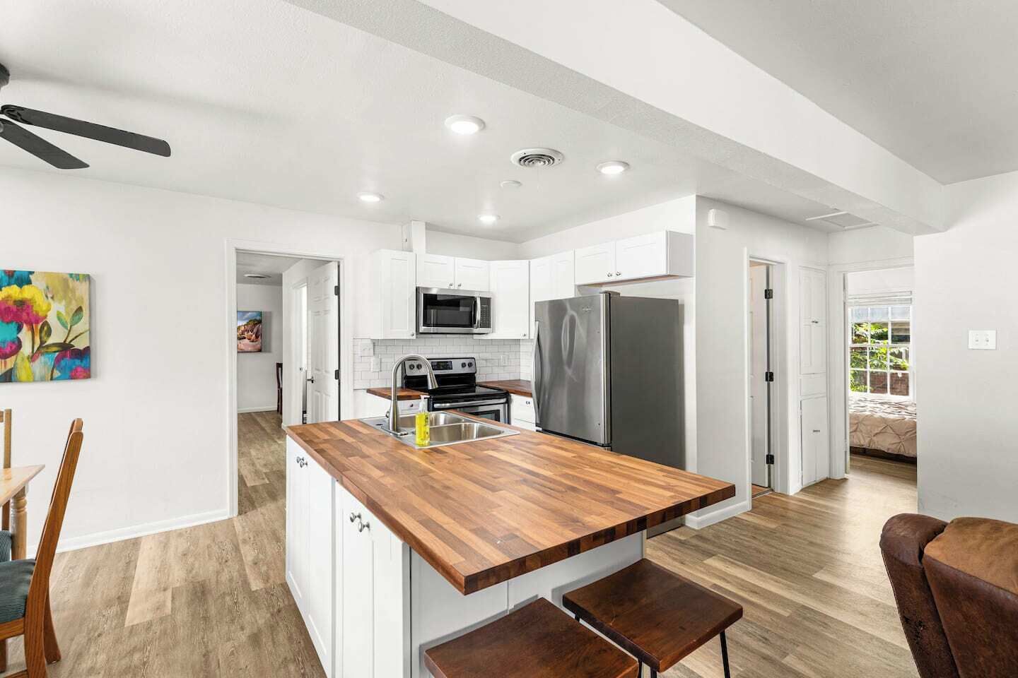 A modern kitchen with white cabinets, a wooden countertop, stainless steel appliances, and a ceiling fan.