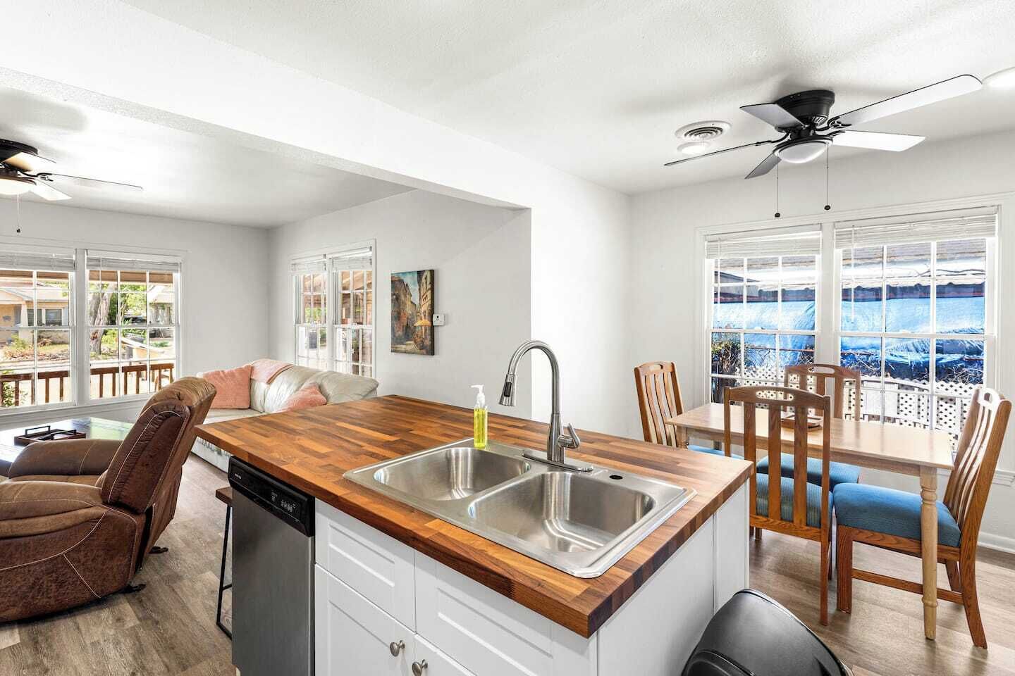 A modern kitchen with a wooden countertop, stainless steel sink, and a dining area with wooden chairs and a table.