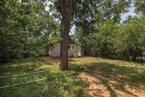 A single-story house with a visible front door and windows, surrounded by dense foliage and a dirt yard. - Modern 3BR Home with Custom Wood Counters (Abilene)
