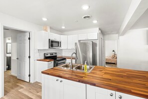 Eine moderne Küche mit weißen Schränken, einem Edelstahlkühlschrank, einer Mikrowelle und einer Holz Arbeitsplatte.