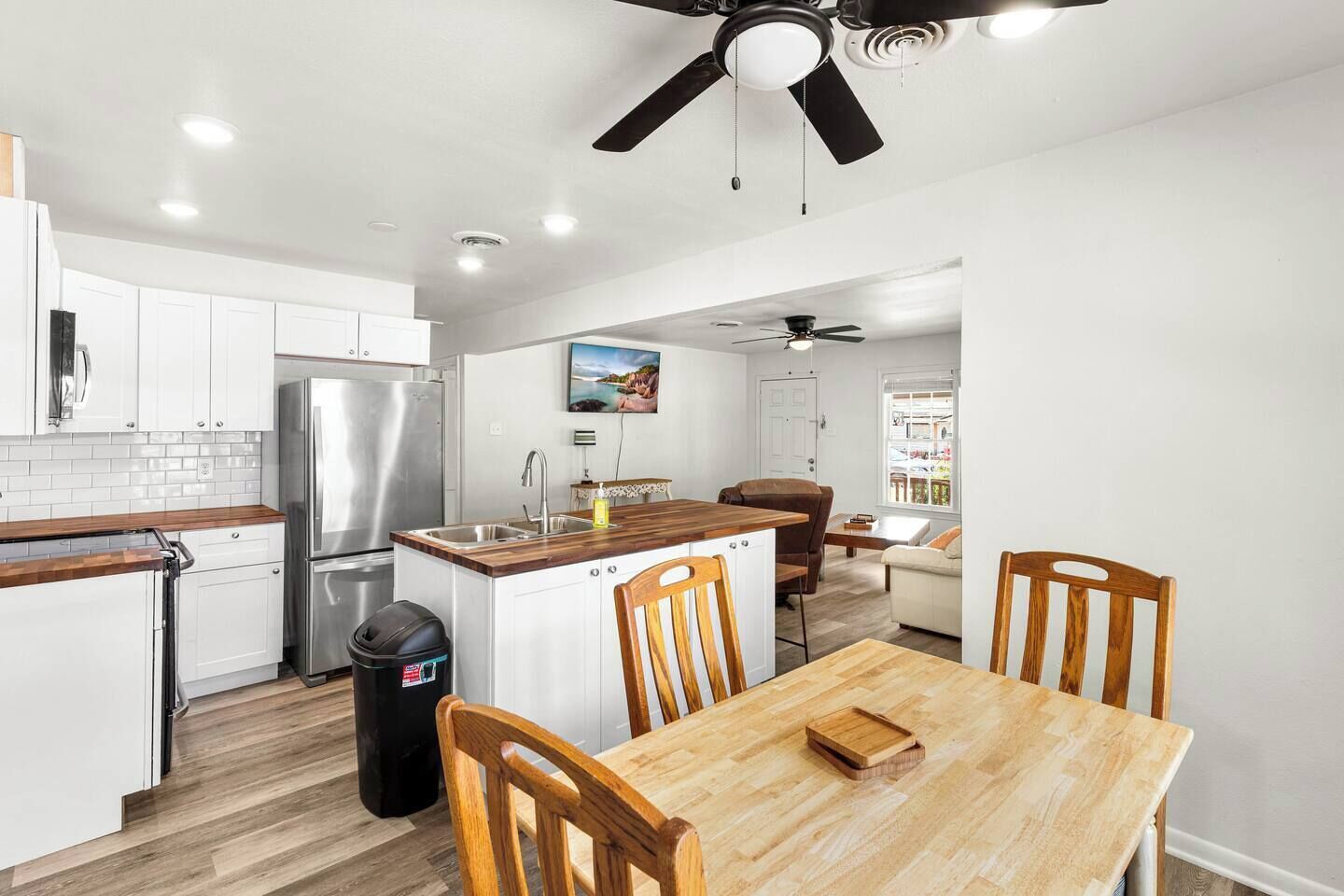 Cocina moderna con armarios blancos, refrigerador de acero inoxidable, encimeras de madera y un comedor con mesa y sillas de madera.
