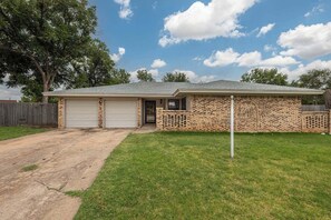 A single-story brick house with a garage, a front lawn, and a wooden fence. - Cozy & Modern 3BR Home with Huge Backyard (Abilene)