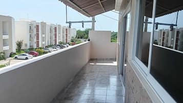 A balcony with a tiled floor, a covered area, and a view of a parking lot with cars.