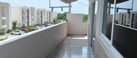 A balcony with a tiled floor, a covered area, and a view of a parking lot with cars.