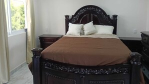 Ein Schlafzimmer mit einem großen Bett, einem Nachttisch, einer Kommode und einem Fenster mit Vorhängen.