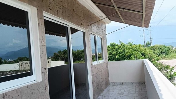 Ein Balkon mit gefliestem Boden, großen Fenstern und Blick auf die Landschaft.