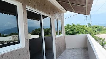 A balcony with a tiled floor, large windows, and a view of the landscape.