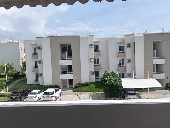 A multi-story residential building with balconies, a parking area, and a clear sky.
