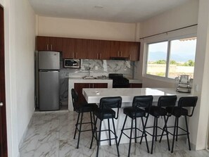 A modern kitchen with marble countertops, a refrigerator, and a dining area with bar stools.