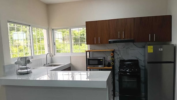A modern kitchen with a central island, stainless steel appliances, and large windows.