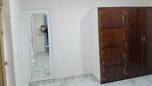 A room with a white door, a wooden wardrobe, and a tiled floor.