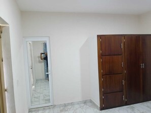 A room with a white door, a wooden wardrobe, and a tiled floor.