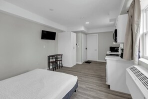 Ein modernes Hotelzimmer mit einem Bett, einem kleinen Tisch, einem Fernseher, einer Küchenzeile und einem Badezimmer.