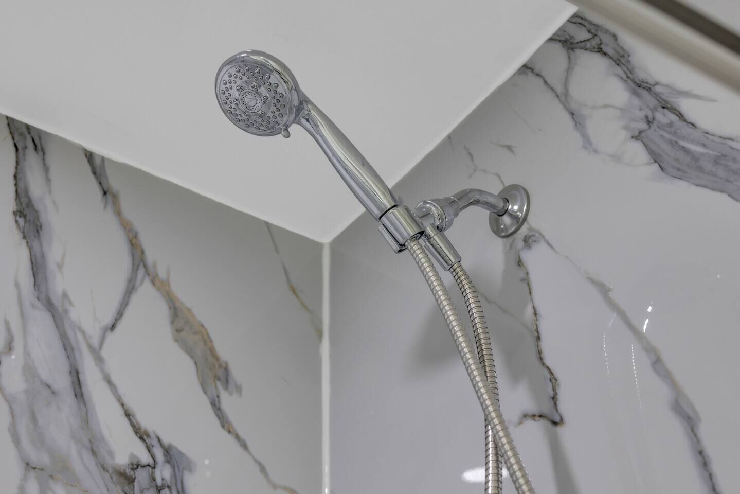 Un cabezal de ducha con manguera flexible, instalado en una pared con diseño de mármol.