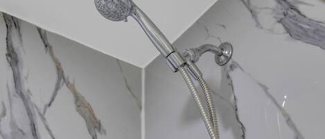 Un cabezal de ducha con manguera flexible, instalado en una pared con diseño de mármol.