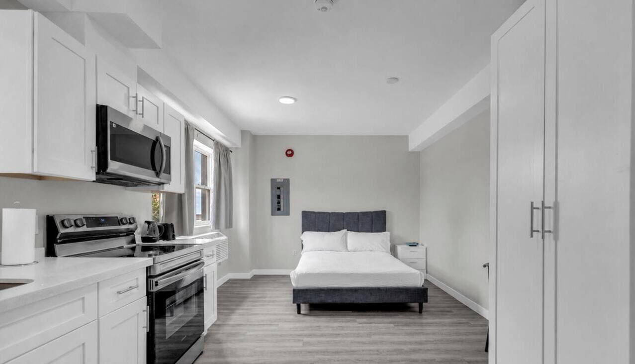Ein kompaktes Hotelzimmer mit Küchenzeile, einem Bett und einem kleinen Nachttisch.