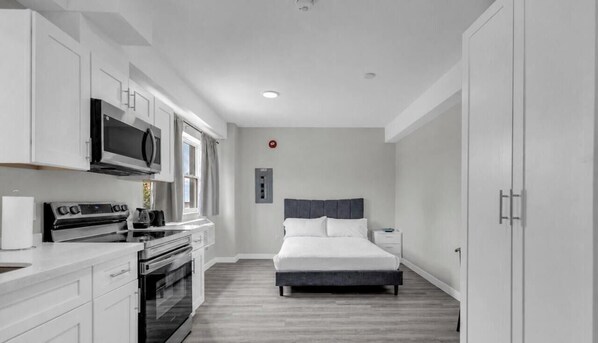Ein kompaktes Hotelzimmer mit Küchenzeile, einem Bett und einem kleinen Nachttisch.