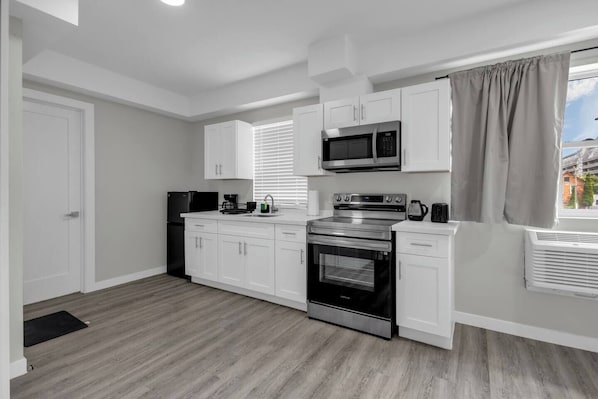 A modern kitchen with white cabinets, a stainless steel microwave, a built-in oven, and a window with blinds.