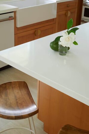 A kitchen with a white countertop, wooden cabinets, and a single white flower in a glass vase. - Modern Island Retreat | Pool & A/C | Mins to Beach (Princeville)