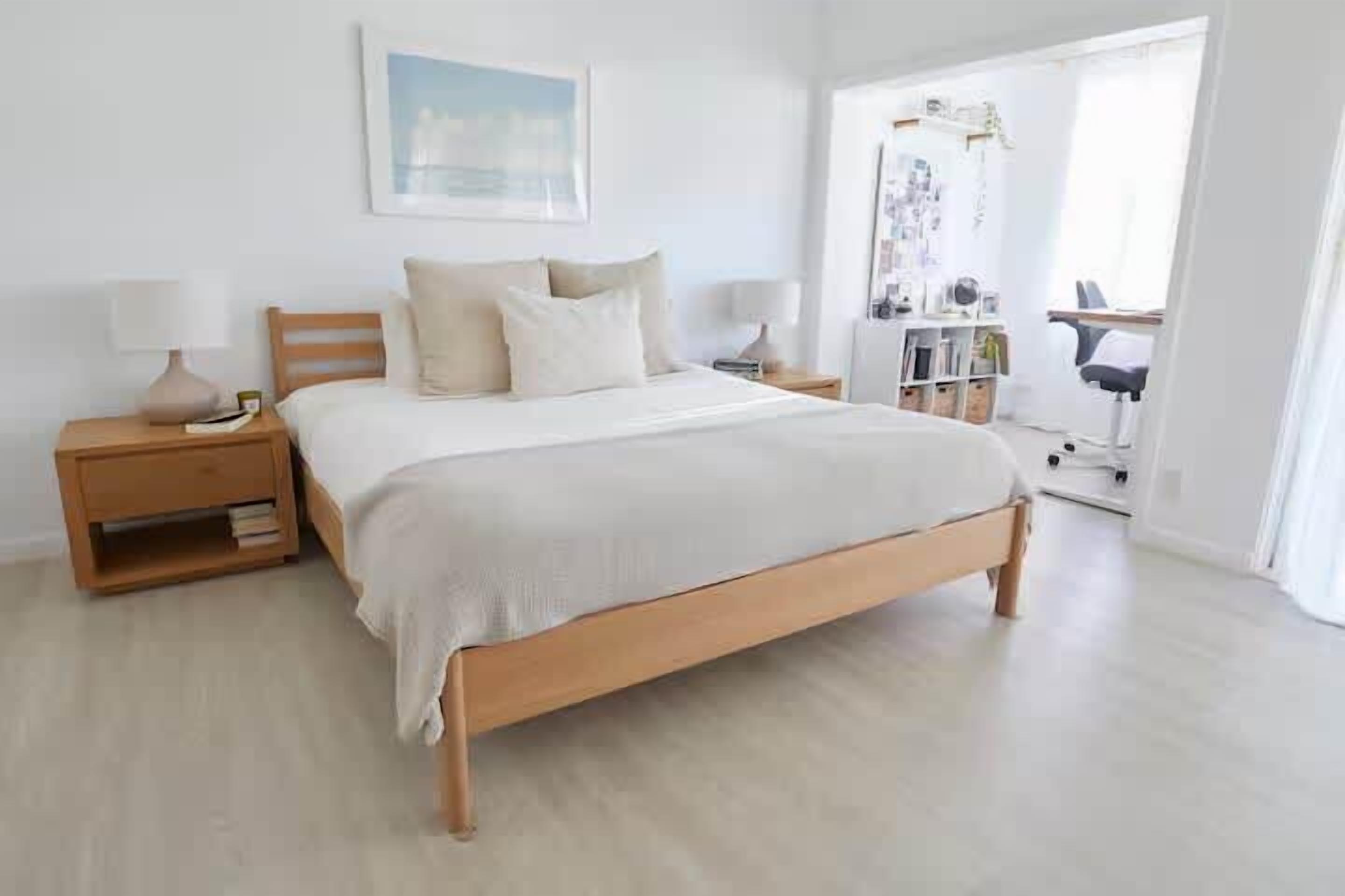 A bedroom with a wooden bed, bedside tables, a nightstand, a desk, and a chair.