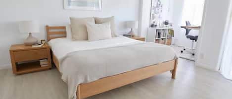 A bedroom with a wooden bed, bedside tables, a nightstand, a desk, and a chair.