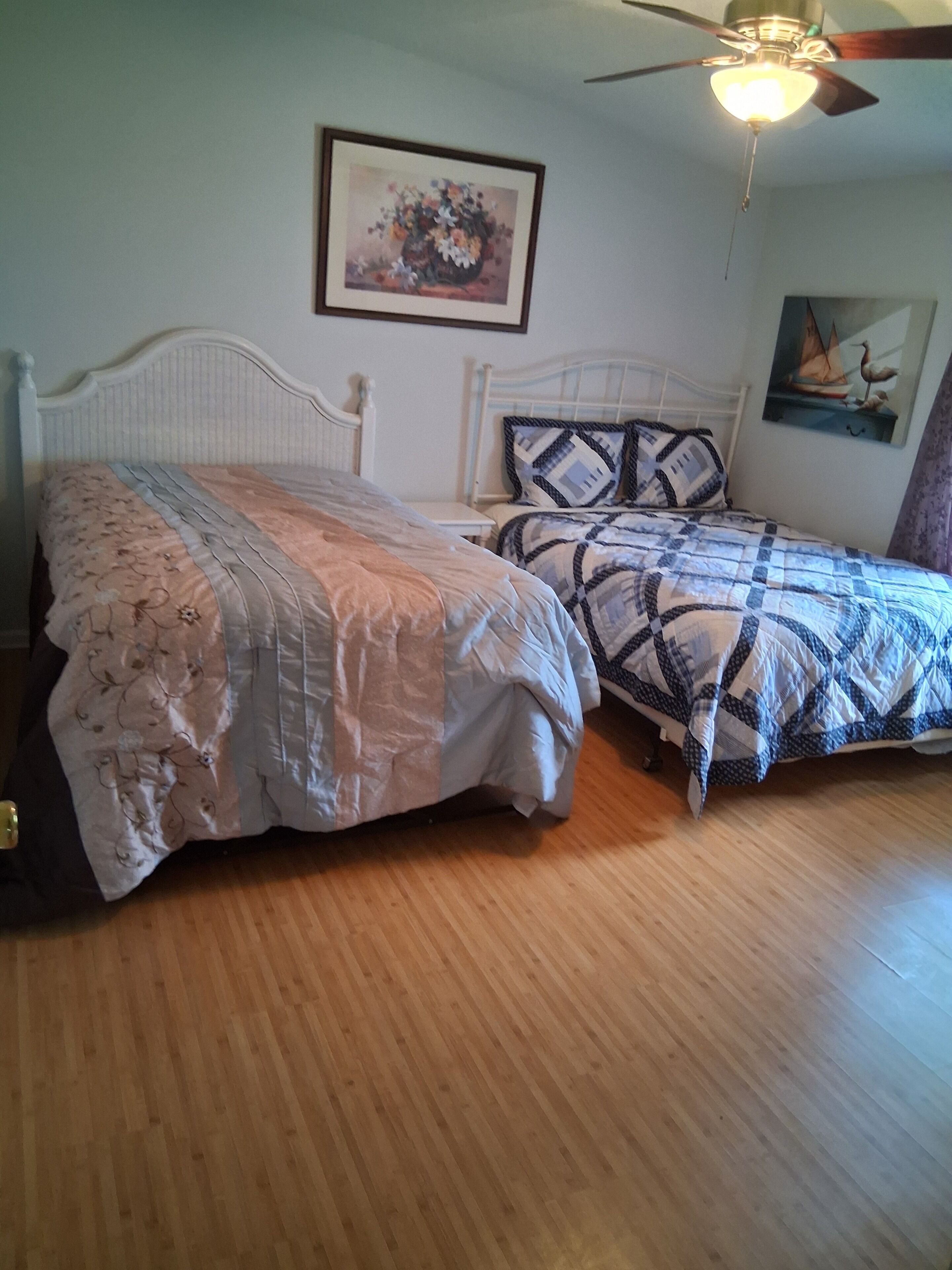 A bedroom with two beds, a ceiling fan, and artwork on the walls.