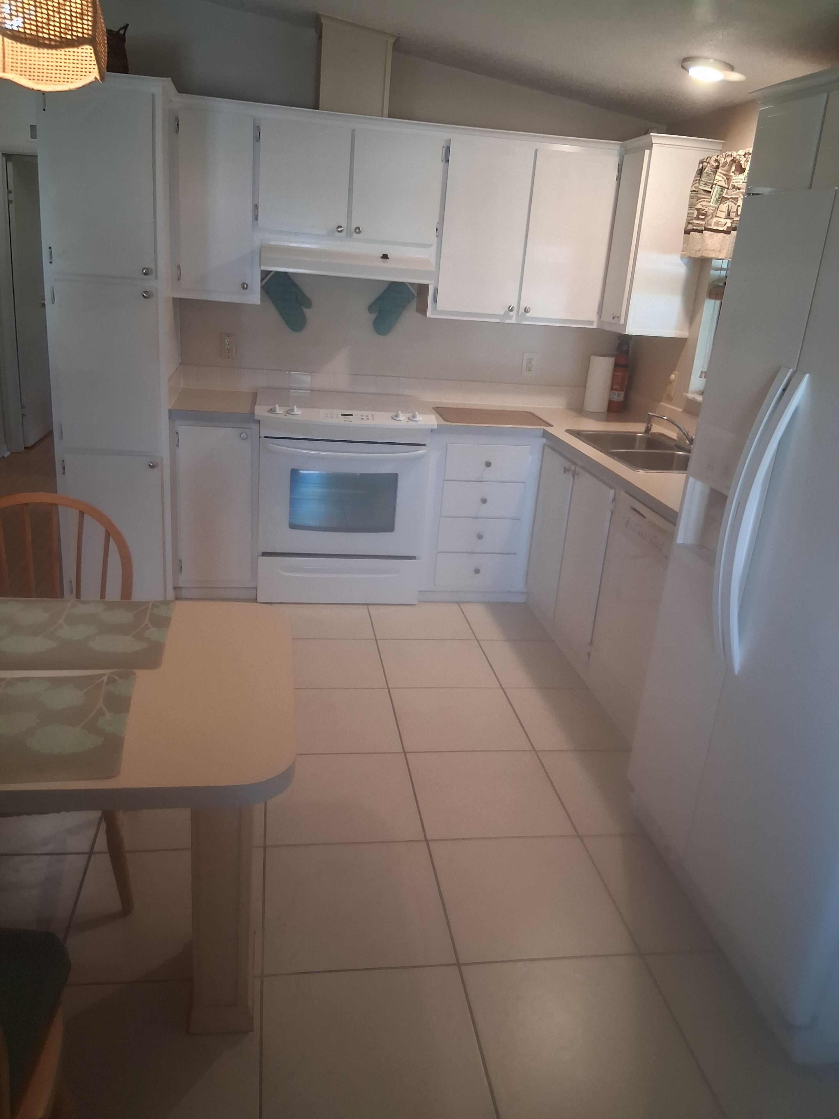 A kitchen with white cabinets, a stove, a sink, and a refrigerator.