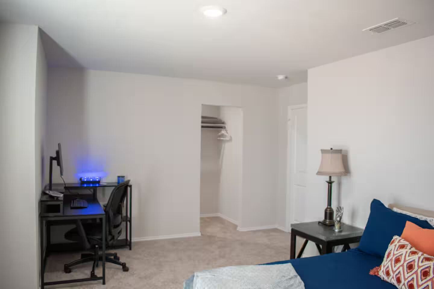 Een slaapkamer met een bed, een bureau met een computer, een lamp en een kast.