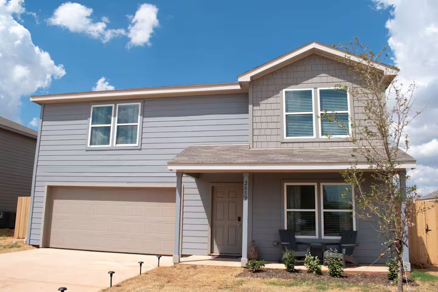 A two-story house with a garage, a front porch, and a small tree.