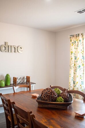 Een eethoek met een houten tafel, stoelen, een decoratieve schaal en een bord met een tekst aan de muur.